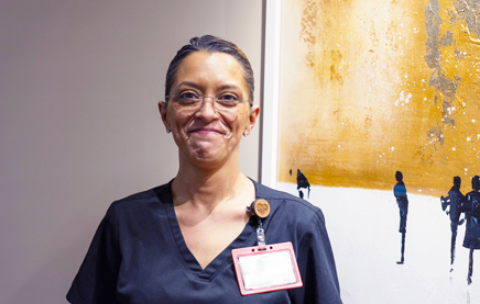 A photograph of a smiling medical assistant standing next to a painting.