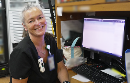 A photograph of a nurse sitting back from her computer workstation, turning to look and smile at the camera