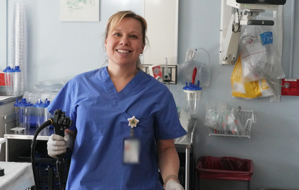 A medical medical lab worker standing in a room with medical equipment, smiling at the camera.