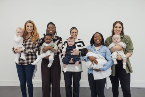 A photograph of a group of five mothers, both bland and white, with their babies.
