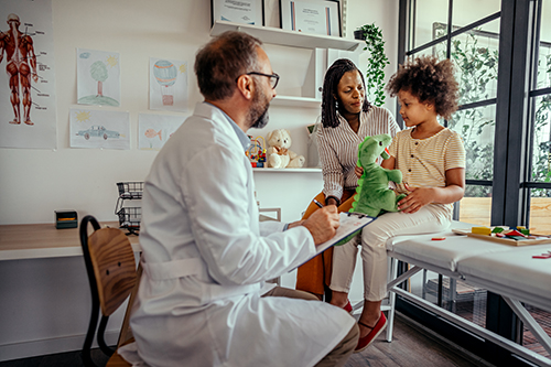 Doctor pediatrician writing information of girl patient in notepad at medical clinic