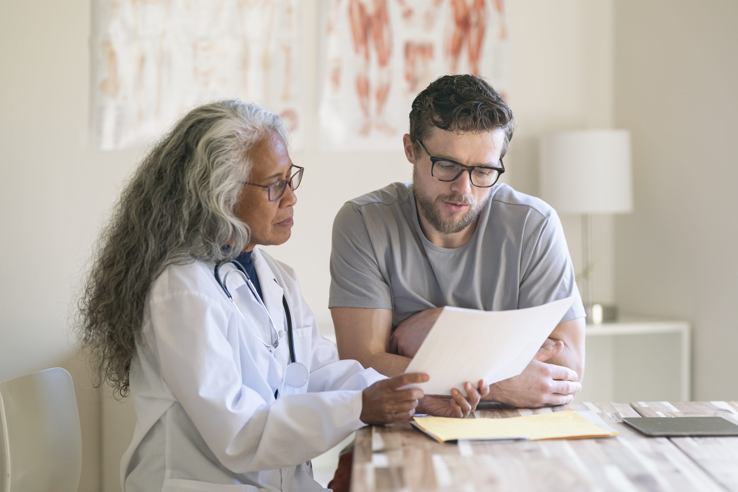 A healthcare provider in a lab coat reviewing a document with a male patient in glasses.