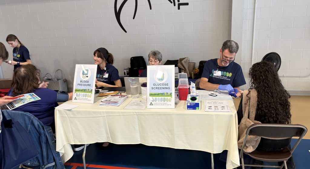 Photo of community members receiving blood pressure and blood glucose screenings from BHS staff.